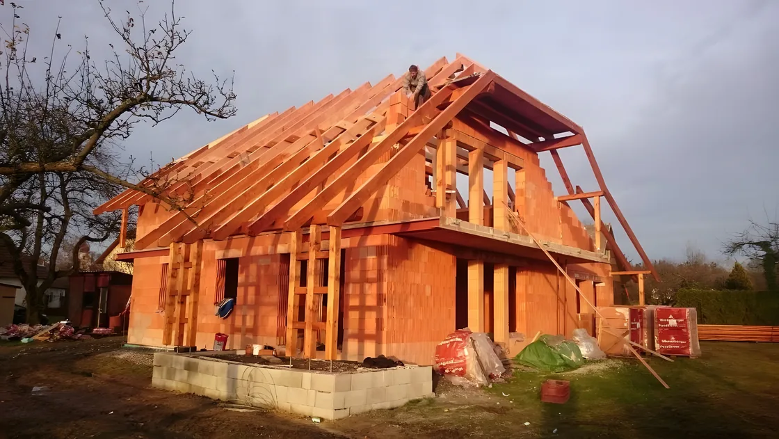 Nový krov s vikýři na cihlové novostavbě, tesař na hřebeni